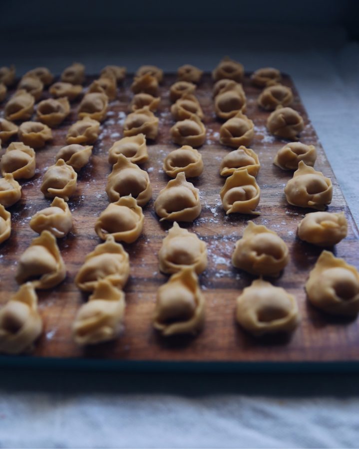 Hand-folded tortellini drying on a wooden board