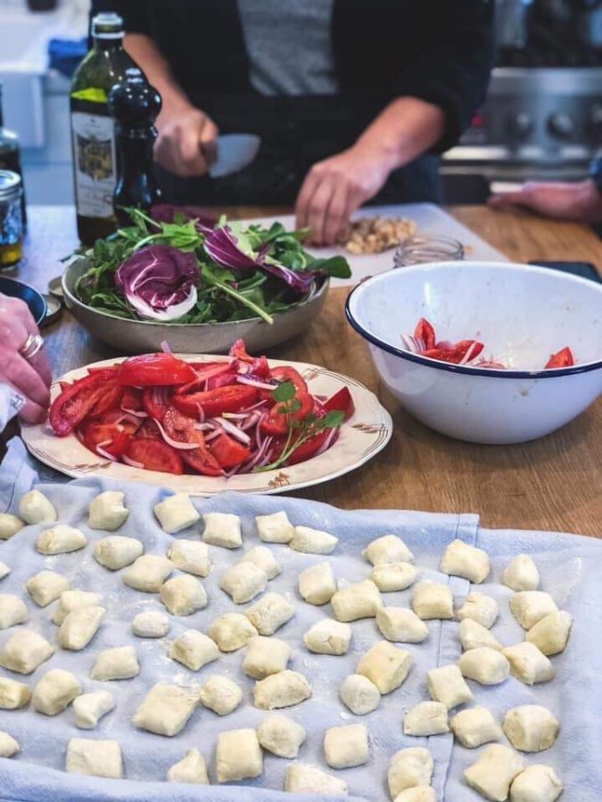 Freshly rolled gnocchi on a tray, with salads and antipasti behind
