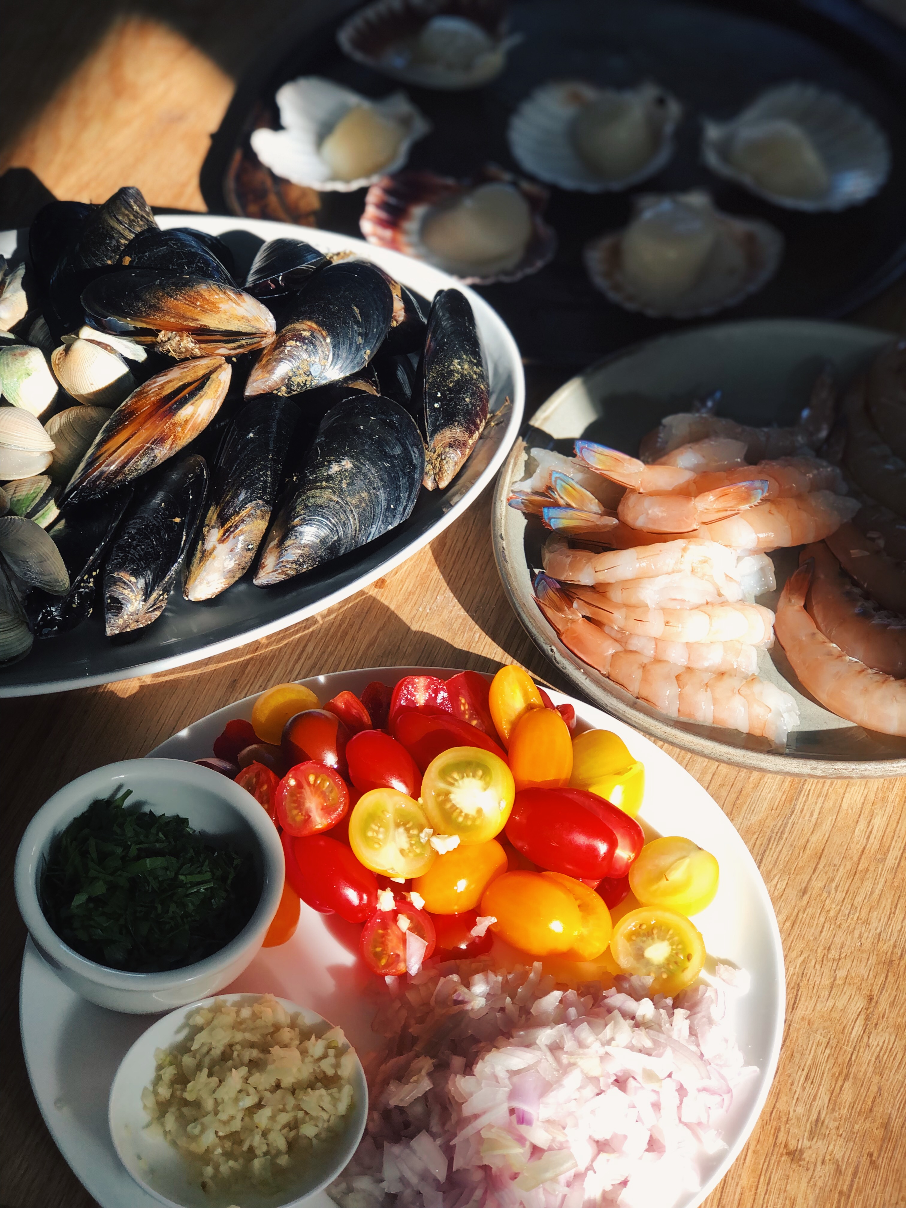 Seafood and aromatics laid out ready to cook — mussels, scallops, prawns and tomatoes