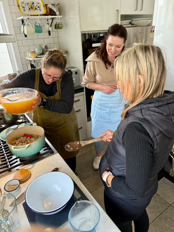 A cooking class in a home kitchen, adding stock to the pot