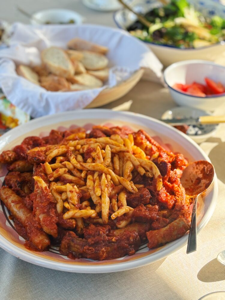 Pasta with a rich tomato ragu and sausage, bread and salad alongside